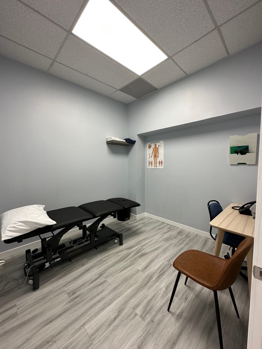 A treatment room with an adjustable table and a spinal nerve chart on the wall